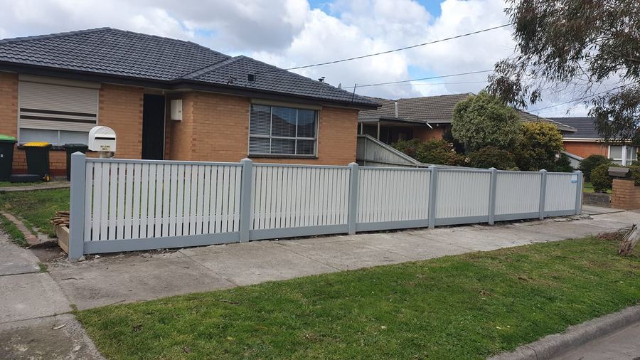 Pale aluminium picket fence along the front of a brick house