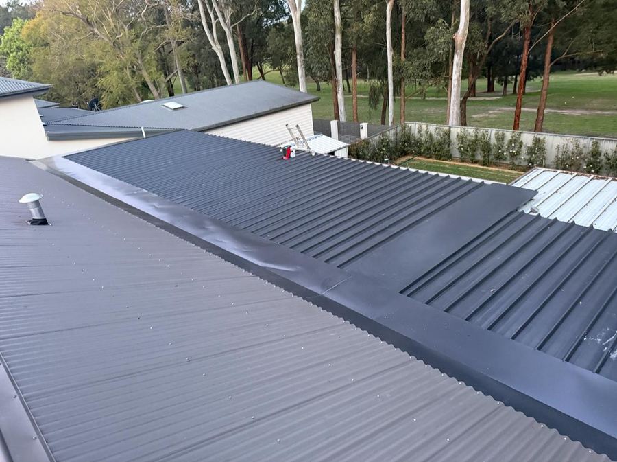 Dark grey corrugated metal roof with a new capping flashing along the join between two roof sections