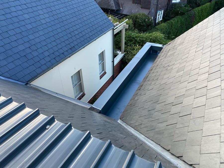 Grey metal box gutter and flashings between slate roof slopes, above a white rendered house