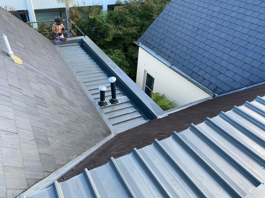 New grey metal tray roof and box gutter running between two slate roofs