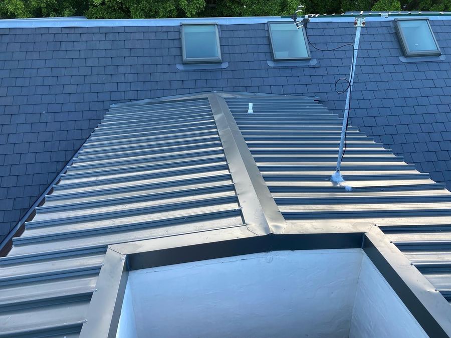 New grey metal tray roof with a raised ridge flashing, set into a slate roof with three skylights