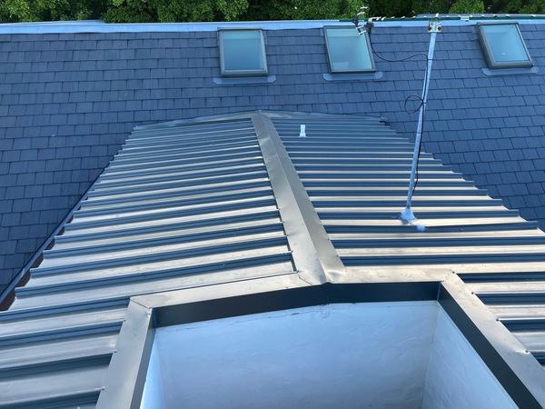 New grey metal tray roof with a raised ridge flashing, set into a slate roof with three skylights