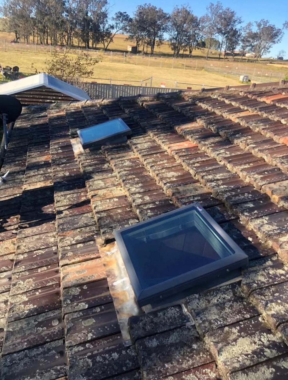 New flat glass skylight fitted into a weathered terracotta tile roof, a second skylight further up the slope