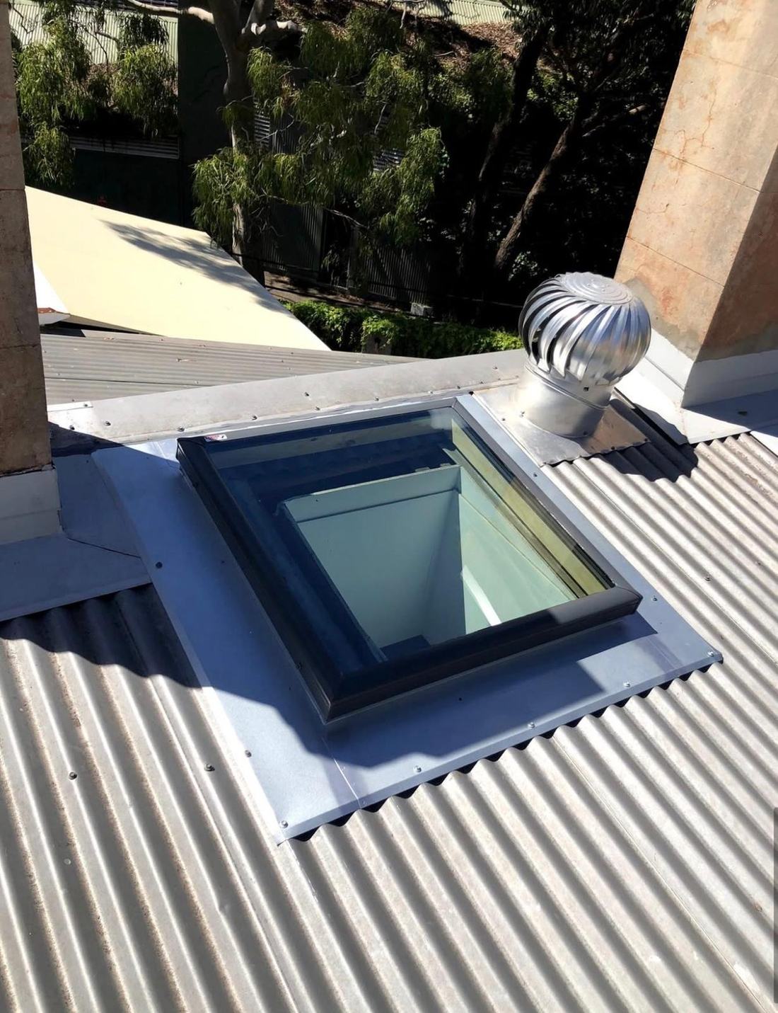 New skylight with fresh metal flashing on a corrugated iron roof, beside a whirlybird vent