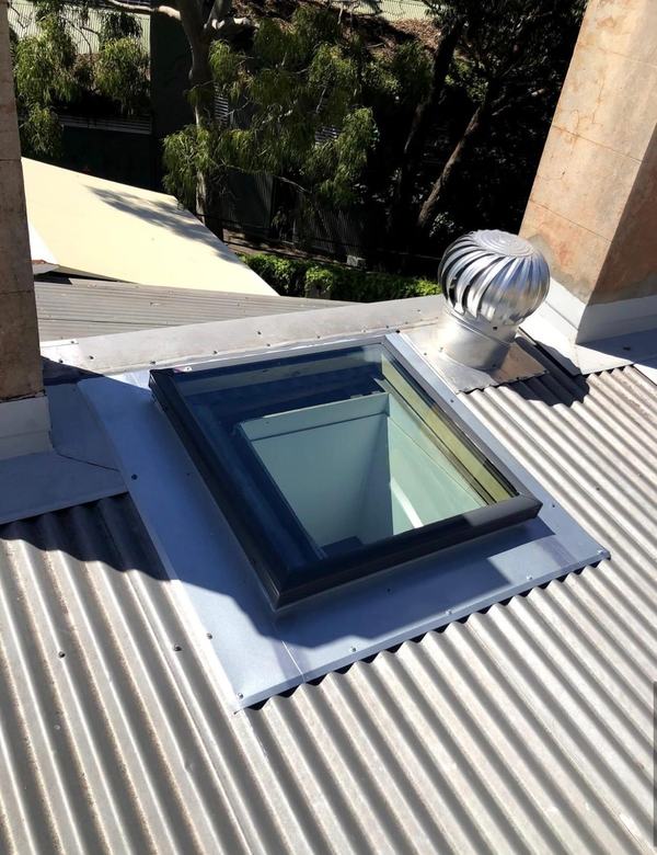 New skylight with fresh metal flashing on a corrugated iron roof, beside a whirlybird vent