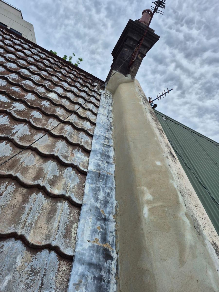 Rendered chimney breast with new flashing along the edge of a terracotta tiled roof